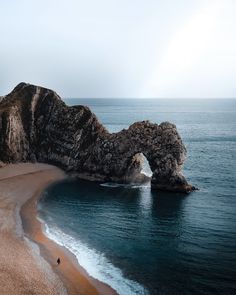 an arch shaped rock sticking out of the ocean next to a sandy beach with waves coming in