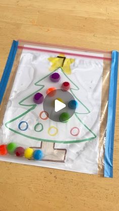 a plastic bag with a christmas tree drawn on it and colored pom poms