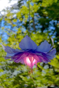 a purple flower hanging from a wire in front of trees