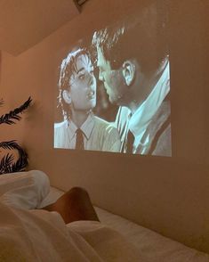 a person laying in bed watching a movie on the wall