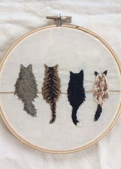 three different colored cats on a white background in a embroidery hoop with the cat's tail hanging down