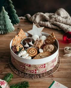 a christmas cookie tin filled with cookies and other holiday treats on a wooden table next to a tree