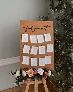 a wooden easer with seating cards attached to it and flowers on the table next to it