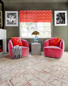 a living room with two pink chairs and a rug in front of a window that has pictures on the wall