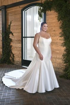 a woman standing in front of a wooden wall wearing a white wedding dress with straps