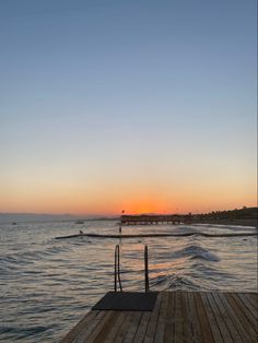 the sun is setting over the water and people are out on the dock in the distance