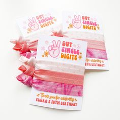 three pink and white hair ties with the words out single digits printed on each one