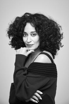 a black and white photo of a woman with curly hair posing for the camera while wearing a sweater