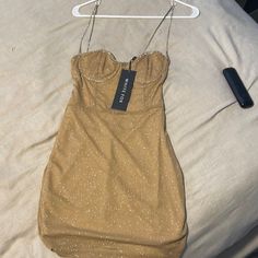 a tan dress hanging on a white hanger next to a remote control and bed