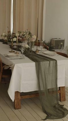 the table is set with white linens and flowers on it, along with two candles