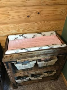 a baby crib with baskets on top of it in front of a wood paneled wall