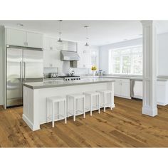 a large kitchen with white cabinets and counter tops, along with four stools in front of the island