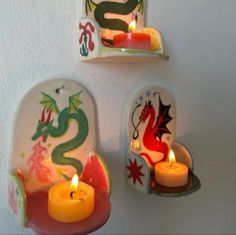 two wall mounted candle holders with dragon designs on them and one holding a lit candle