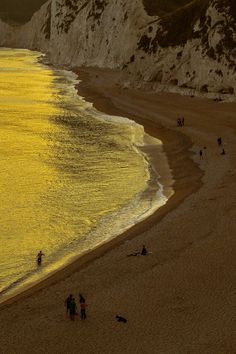 people are walking on the beach near the water's edge and cliffs in the background