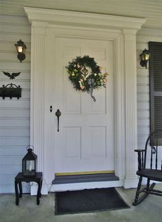 a white door with a wreath and two rocking chairs