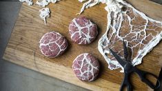 three raw meat patties sitting on top of a cutting board next to a pair of scissors