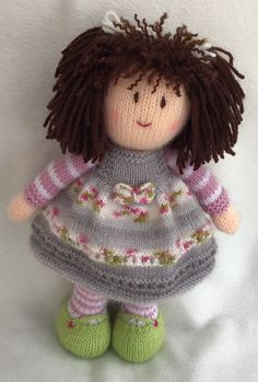 a knitted doll with brown hair wearing a gray dress and green shoes on a white surface