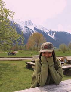 a woman sitting at a picnic table with her hands on her face and mountains in the background