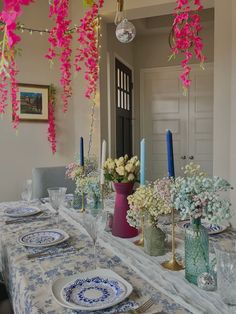 the table is set with blue and white dishes, candles, and flowers in vases