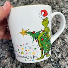 a hand holding a coffee mug with the grinch on it's side and saying merry christmas at lot