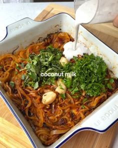 someone pouring milk into a dish of noodles and vegetables in a blue and white casserole