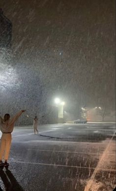 two people standing in the snow at night with their arms up and one person holding an umbrella