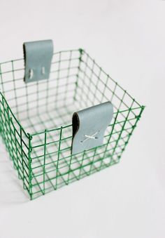 a green wire basket with two rolls of toilet paper in it on a white surface