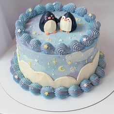 there is a cake with two penguins on top and blue icing around the edges