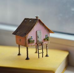 a miniature house on top of a book with a ladder to the roof and windows