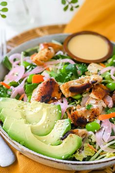 a salad with chicken, lettuce, carrots and avocado in a bowl