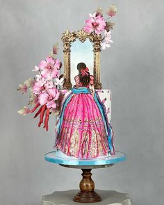 a cake decorated with flowers and an image of a woman in a pink dress sitting on top of a table