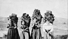 three women in long dresses are standing on a hill with large headpieces over their heads