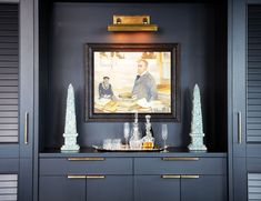 a painting hangs on the wall above a cabinet with glass vases and other items