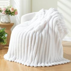 a white blanket sitting on top of a wooden floor next to a potted plant