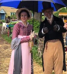 a man and woman dressed up in period clothing under an umbrella while standing next to each other