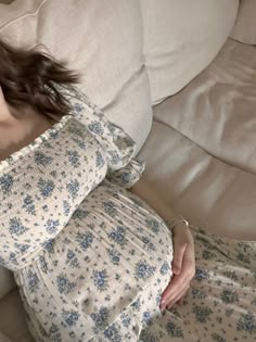 a woman laying on top of a white couch next to pillows with blue flowers all over it