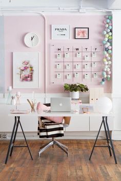 a desk with a laptop on it in front of a pink wall and calendars