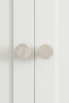 two white cupboards with marble knobs on the doors and one has a round door handle