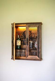 a wooden cabinet with wine glasses and bottles in it on the wall next to a white wall