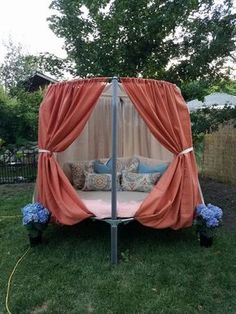 an outdoor bed with drapes and flowers on the grass in front of a fence