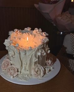 a white cake with frosting and flowers on it sitting on a table next to a lit candle