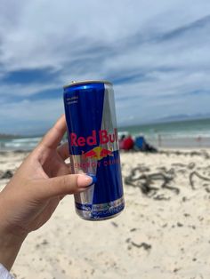 a person holding up a red bull energy drink on the beach