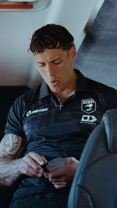 a man sitting on an airplane looking at his cell phone while holding a pair of cards