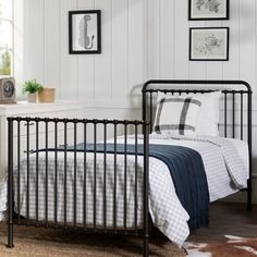 a black metal bed frame with checkered sheets and pillows in a white bedroom setting