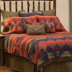 a bed with an orange and blue blanket on top of it next to a wooden headboard