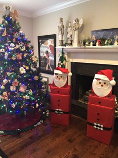 two santa clause boxes sitting next to a christmas tree in front of a fire place