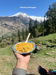 someone holding up a plate of macaroni and cheese in front of the mountains