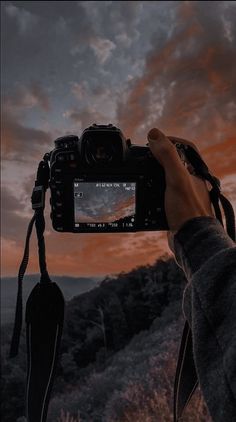 a person holding up a camera to take a photo at sunset or dawn with the sky in the background