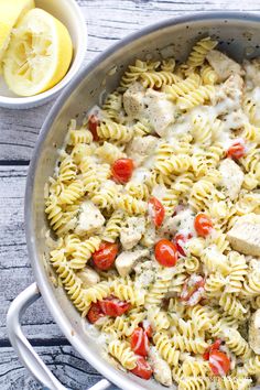 a pan filled with pasta and chicken covered in sauce next to a lemon wedge on the side