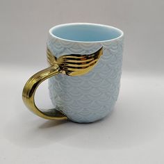 a blue and white coffee cup with gold handles on the handle is shaped like a fish's tail